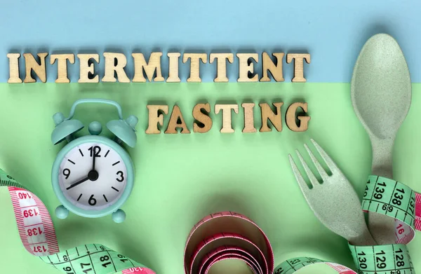 Diyet ve kilo verme konsepti: saat, kaşık ve çatal. Aralıklı oruç kelimesi ahşap harflerden geliyor. Düzgün beslenme kavramı. Düz yat, boşluğu kopyala.