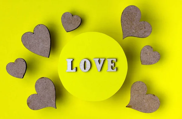 Hearts and word love made from wooden letters. Yellow background. The concept of holidays and love.  Flat lay, copy space.
