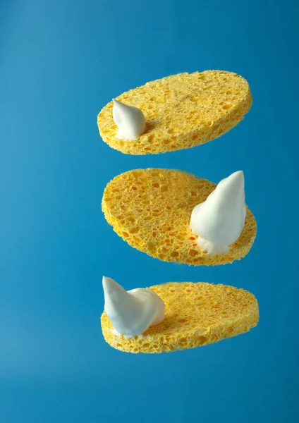 Natural yellow cosmetic sponges with cleansing foam on blue background. Morning or evening beauty routine. Concept of beauty care for the face. Copy space.
