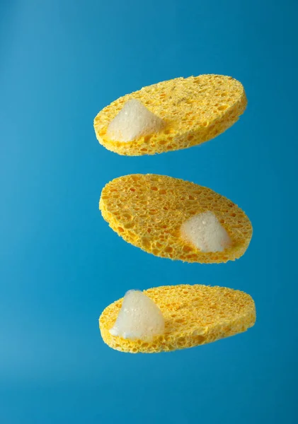 Natural yellow cosmetic sponges with cleansing foam on blue background. Morning or evening beauty routine. Concept of beauty care for the face. Copy space.