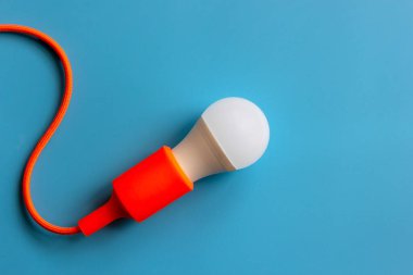 Mavi arka planda turuncu kablosu olan bir ampul açık. Yaratıcı fikirler kavramı.