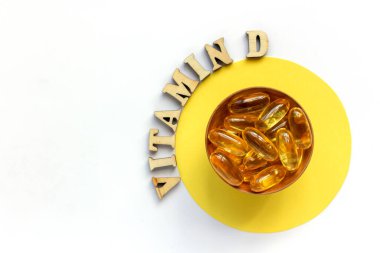 Küçük bir tabakta sarı haplar ya da tabletler. D vitamini harfleri ahşap harflerle kaplıdır. Sağlık konsepti. Düz yat, boşluğu kopyala.