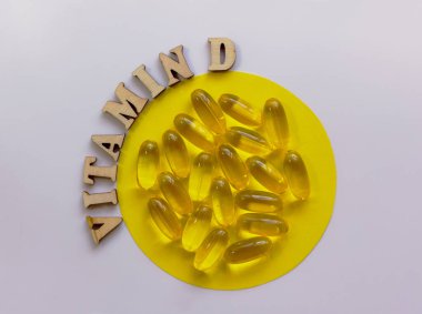 Küçük bir tabakta sarı haplar ya da tabletler. D vitamini harfleri ahşap harflerle kaplıdır. Sağlık konsepti. Düz yat, boşluğu kopyala.