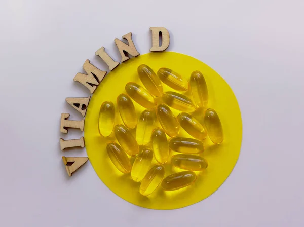 Küçük bir tabakta sarı haplar ya da tabletler. D vitamini harfleri ahşap harflerle kaplıdır. Sağlık konsepti. Düz yat, boşluğu kopyala.