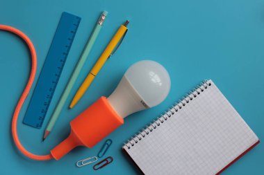 Mavi arka planda ampul, not defteri, kalem ve kalemi olan yaratıcı bir düzen. İş, proje veya beyin fırtınası için yaratıcı fikir.