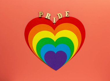 Gökkuşağı İşitmeleri pembe arka planda gey ve LGBT gururunu sembolize eder. Tahta harflerden yapılmış bir kelime - Gururlu.