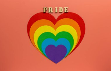 Gökkuşağı İşitmeleri pembe arka planda gey ve LGBT gururunu sembolize eder. Tahta harflerden yapılmış bir kelime - Gururlu.