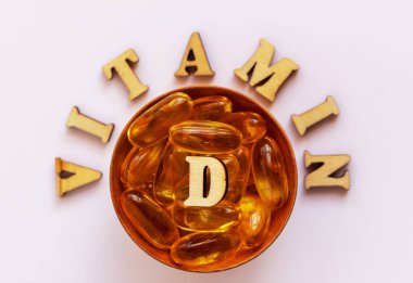 Küçük bir tabakta sarı haplar ya da tabletler. D vitamini harfleri ahşap harflerle kaplıdır. Sağlık konsepti. Düz yat, boşluğu kopyala.