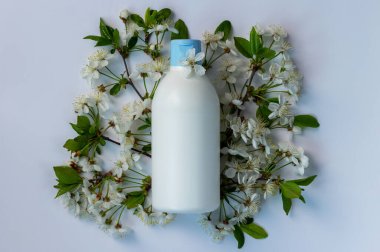 Etiketsiz plastik kozmetik şişesi ve beyaz arka planda bahar çiçekleri olan meyve ağaçları. Güzellik ve cilt bakımı. Kopyalama alanı olan spa arkaplanı.