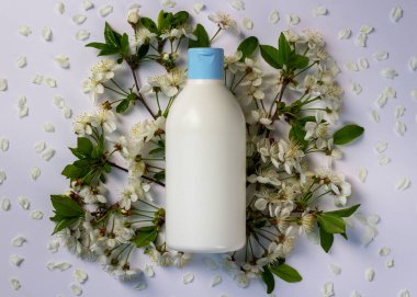 Etiketsiz plastik kozmetik şişesi ve beyaz arka planda bahar çiçekleri olan meyve ağaçları. Güzellik ve cilt bakımı. Ürün için maket. Kopyalama alanı olan spa arkaplanı.