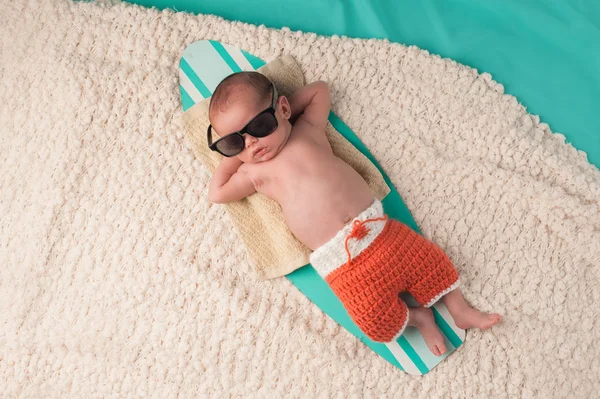 Menino recém-nascido dormindo em uma prancha de surf — Fotografia de Stock