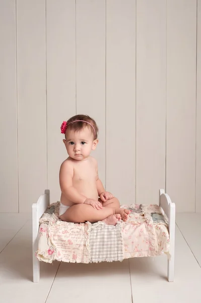 Baby flicka sitter på en liten säng — Stockfoto
