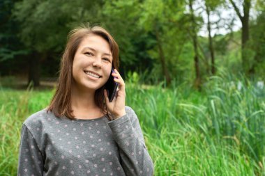 mutlu genç kadın ormanda telefonda konuşuyor