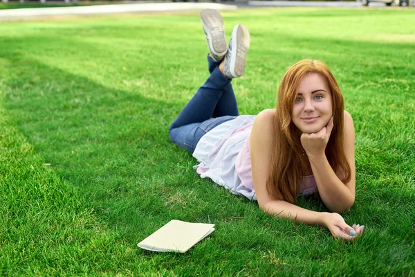 Mujer acostada en un césped con un diario — Foto de Stock