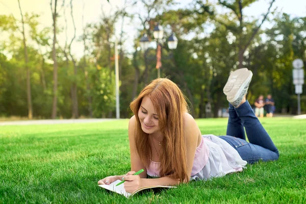 Mujer acostada en un césped con un diario — Foto de Stock