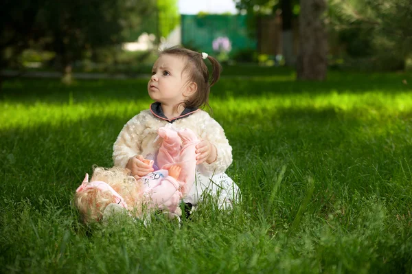 Ein kleines Mädchen sitzt auf dem Gras, während sie mit Puppe spielt — Stockfoto