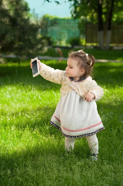 Ein kleines Mädchen spielt im Park mit dem Handy — Stockfoto