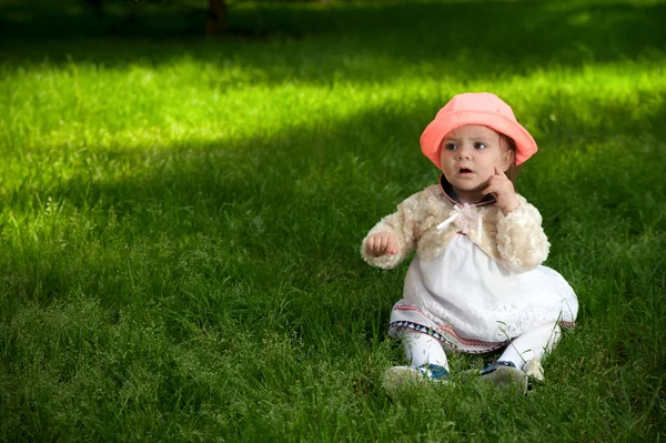 Ein kleines Baby mit hellem Hut sitzt auf dem Gras — Stockfoto