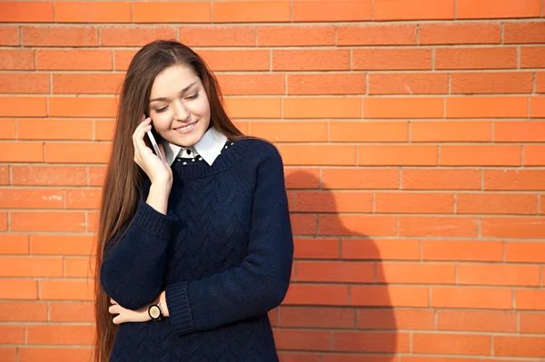 Young woman talking on the phone on a red wall — Stock Photo, Image