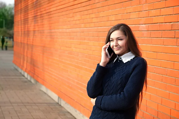 Young woman talking on the phone on a red wall — Stock Photo, Image