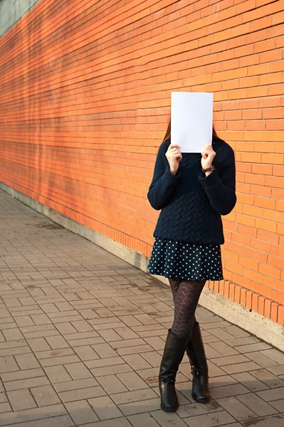 A young woman holds a piece of paper near the face — Stock Photo, Image