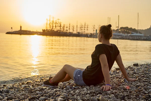 Mujer sentada en la playa y mirando el atardecer — Foto de Stock