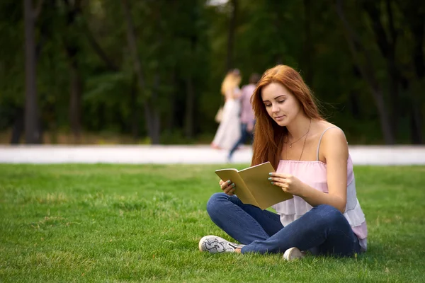 Mujer sentada en el césped y leyendo — Foto de Stock