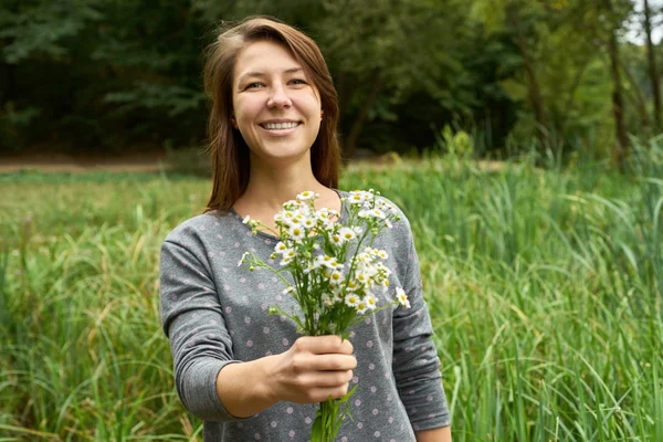 smiling woman presents a bouquet of daisies