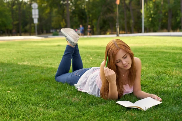 Mujer acostada en la hierba y enseña lecciones — Foto de Stock