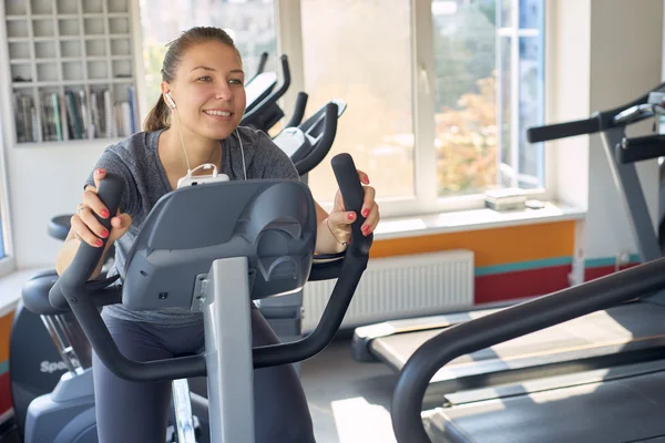 Lycklig kvinna är engagerad på en stillastående cykel — Stockfoto