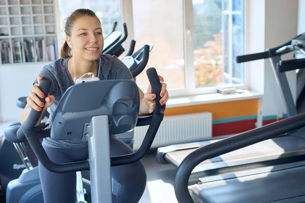 Lycklig kvinna är engagerad på en stillastående cykel — Stockfoto