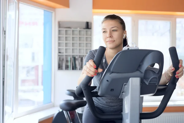 Lycklig kvinna är engagerad på en stillastående cykel — Stockfoto