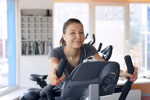 Lycklig kvinna är engagerad på en stillastående cykel — Stockfoto