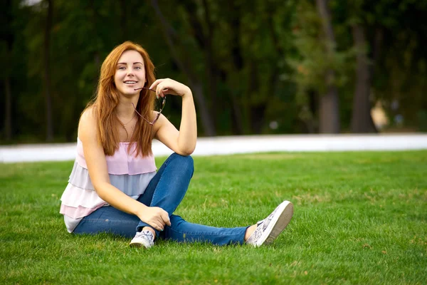 Beautiful woman sitting on the lawn in the park — Stock Photo, Image