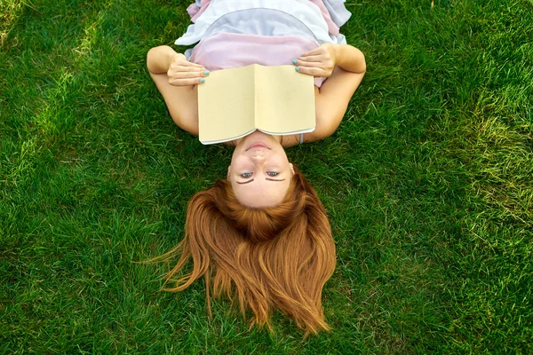 Mujer acostada en un césped con un diario — Foto de Stock