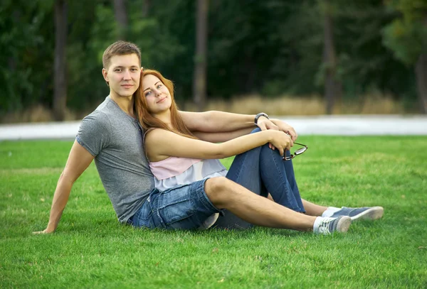 Pareja joven sentada en el césped en el parque — Foto de Stock