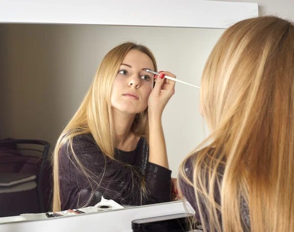 Reflejo de una joven hermosa mujer que se aplica el maquillaje, mirando en un espejo — Foto de Stock