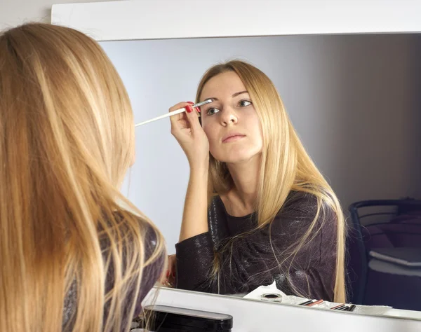 Reflejo de una joven hermosa mujer que se aplica el maquillaje, mirando en un espejo — Foto de Stock