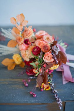 Portakal, kırmızı çiçek ve böğürtlenli güzel bir sonbahar buketi. Ahşap bir masada kurdeleli sonbahar buketi.