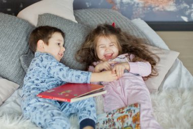 Küçük çocuk ve pijamalı kız yatakta uzanıp Noel ağacının yanında ışık saçan kitaplar okuyorlar. Tatlı Noel çocukları.