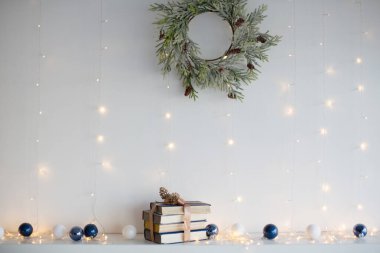 Kurdeleli kitaplar, Noel baloları, Noel çelenkleri ve beyaz duvarın yanındaki Noel ışıkları.