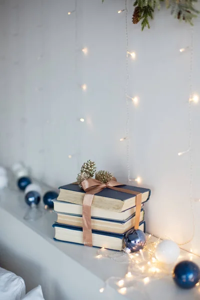 Kurdeleli kitaplar, Noel topları ve beyaz duvarın yanında Noel ışıkları.