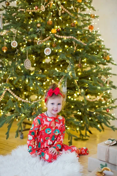 Cute Little Girl Red Pajamas Sits Christmas Tree Decorations Lights — Stock Photo, Image