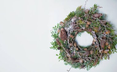 Beyaz arka planda Noel çelengi. Çam kozalaklı, fındıklı, dallı ve yeşil yapraklı doğal çelenk.