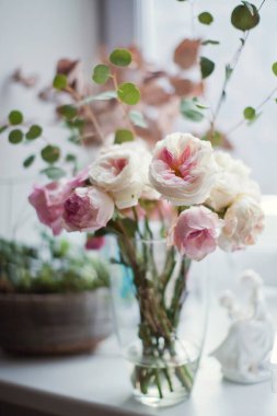 Pencere kenarındaki cam vazoda pembe ve beyaz güller ve okaliptüs.