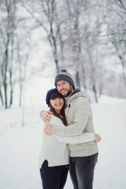 Kar ormanında genç beyaz bir çift. Erkek ve kadın kış gününde yürüyorlar