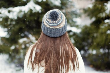 Örgü şapkalı esmer kadın kış ormanlarında kar ağaçlarına bakıyor.