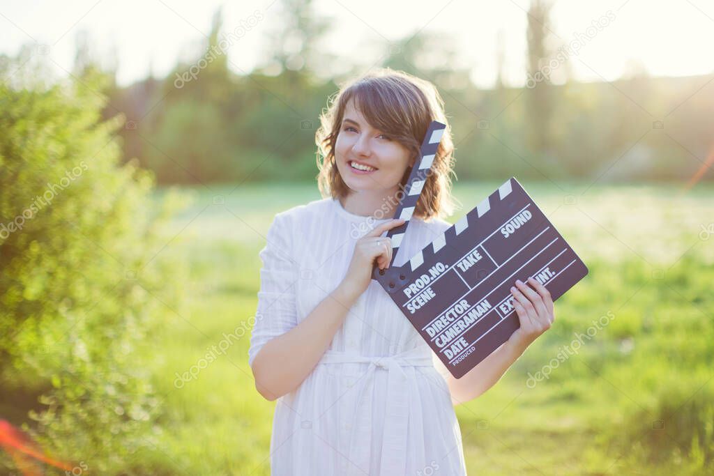 Beautiful caucasian woman holds clapper board at sunset light