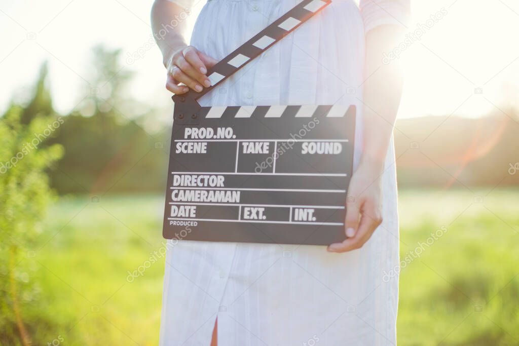 Beautiful caucasian woman holds clapper board at sunset light