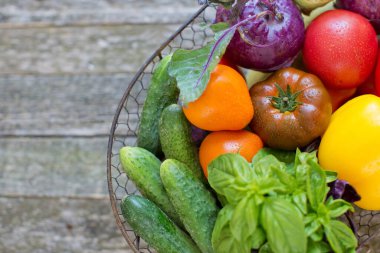 Eski ahşap arka planda taze sebzeli metal sepet. Taze biber, domates, salatalık, fesleğen yaprağı ve metal sepette kohlrabi.
